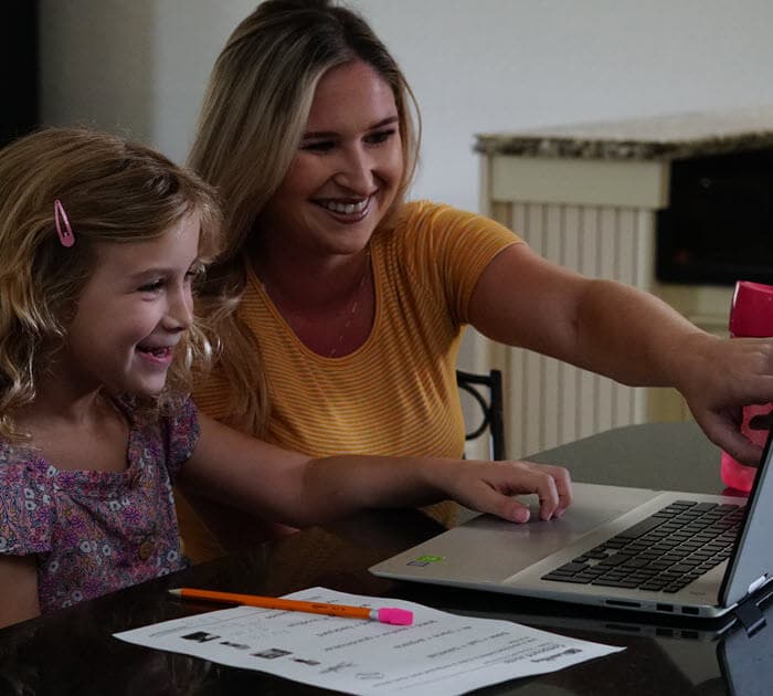 A mother and her dauther pointing at the laptop screen during an online lesson
