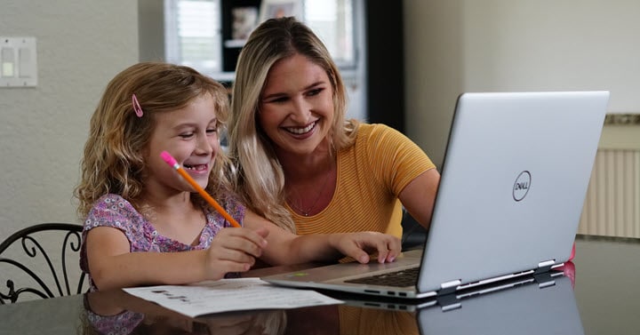 A mother is happily helping her daughter take notes for an online lesson