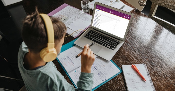 A young student is wearing headphones and participating in an online school lesson