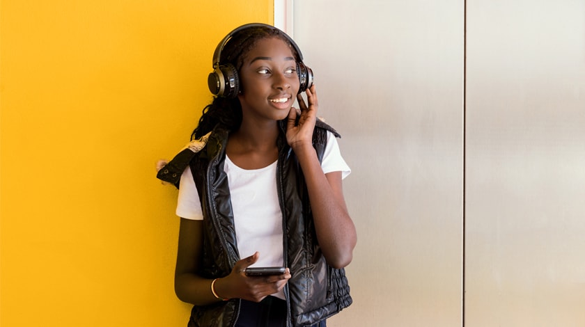 A teenage girl standing against a wall listening to headphones