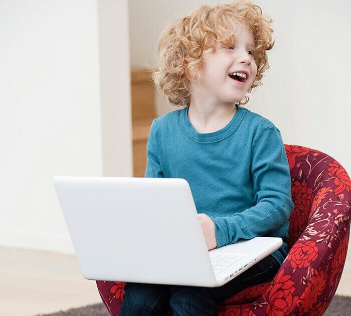 Young Caucasian boy sits in chair with laptop