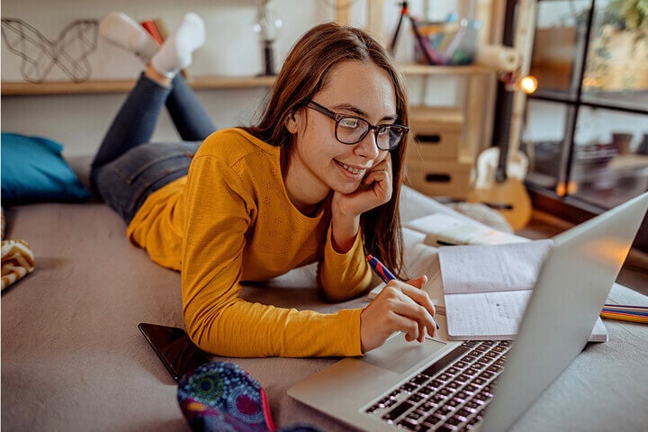 A teenage girl laying on the floor looking at a laptop