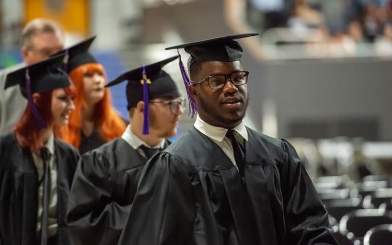 A group of graduating students from Alabama Connections Academy wearing black caps and gowns, walking in a procession.