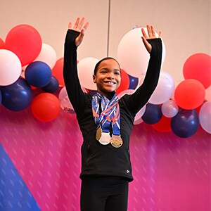 Image of Jaysha M., a student at Arizona Connections Academy, at a gymnastics meet podium wearing several medals.