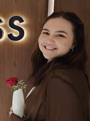 Image of Lacy M wearing a brown sweater and holding a flower vase with a red rose. 