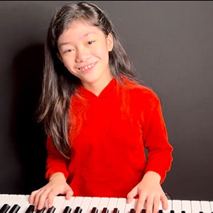 Image of Ardyanna Ducusin in a red shirt playing the keyboard.
