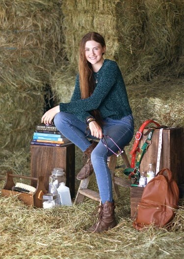 Image of Grace Davis, a senior at Colorado Connections Academy wearing a green sweater sitting on a bale of hay. 