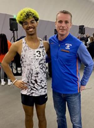 Image of Aaron from Indiana Connections Academy smiling here in a white and black tank top with his track coach. 