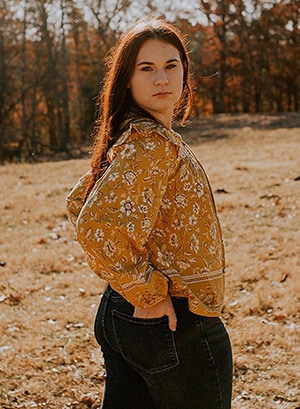 Image of Allayna L. pictured here in an orange shirt in a field. She is a student at Indiana Connections Career Academy. 