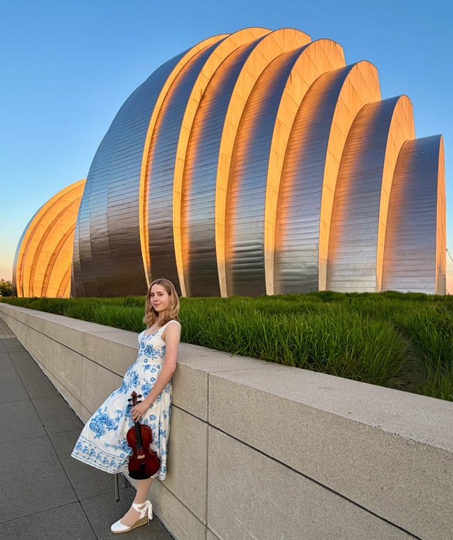 Bridget holding a violin in front of the Youth Symphony of Kansas City
