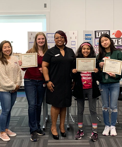 A teacher standing next to her students who are holding certificates