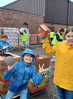 Image of Emberley, Lincoln, and Myles Miller helping to unload food at a food bank.