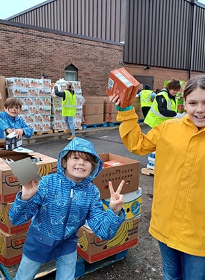 Image of Emberley, Lincoln, and Myles Miller helping to unload food at a food bank. 