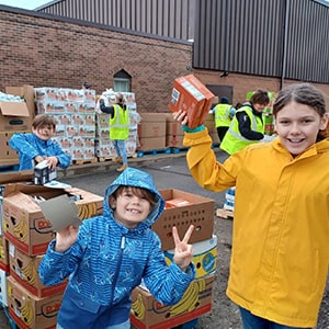 Image of Emberley, Lincoln, and Myles working at a food bank helping to unpack food. 
