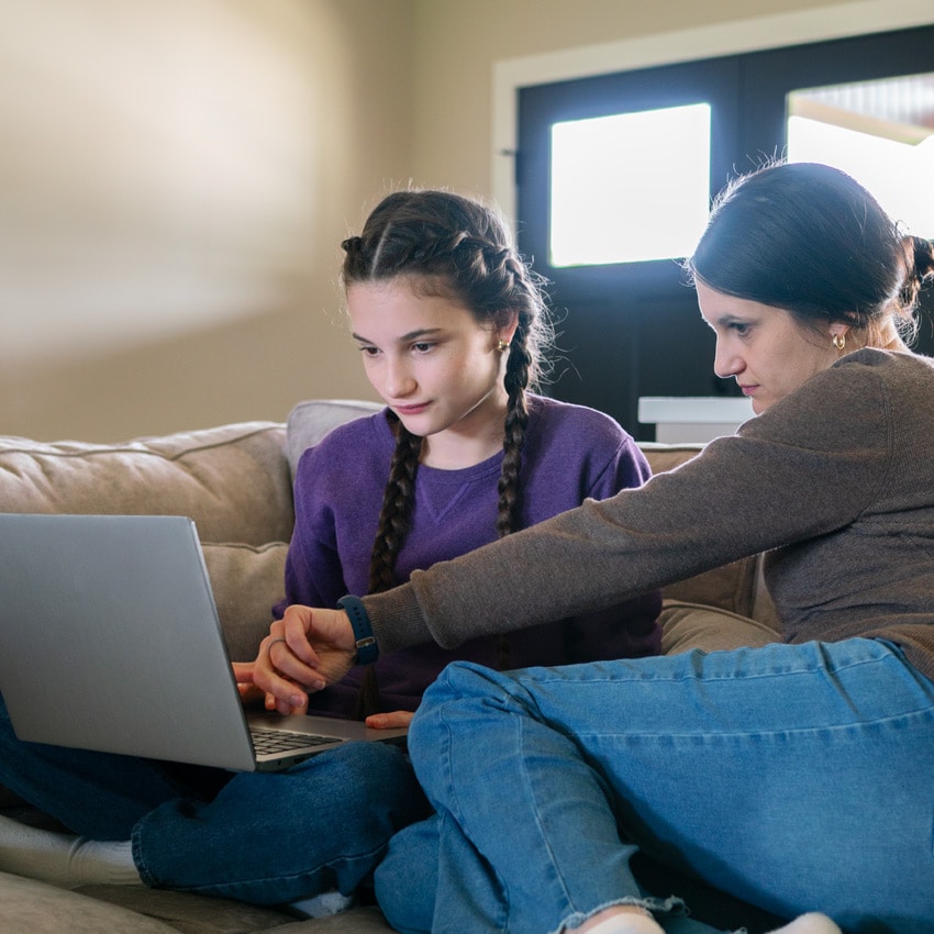 Missouri Connections Academy, Ella, and her Learning Coach sit together on a couch, working on online school assignments using a laptop.