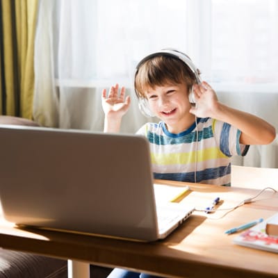 A young first grade Connections Academy student smiling and waving at his laptop