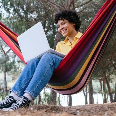 A teen student in an yellow shirt sitting on a colorful hammock outside taking a math class at Connections Academy
