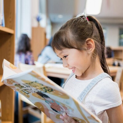 A young first grade Connections Academy student reading a book at a library. 