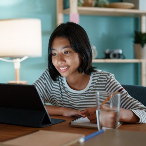 A young teen in a black and white sweater smiling at the camera while taking an class at Connections Academy. 