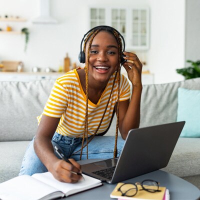 A teen student in an yellow shirt sitting on a white sofa working on an online Algebra 2 class for Connections Academy.