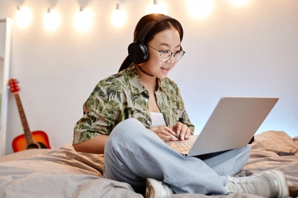 Teen female student in an camo shirt sitting on their bed working on an online science assignment for Connections Academy.