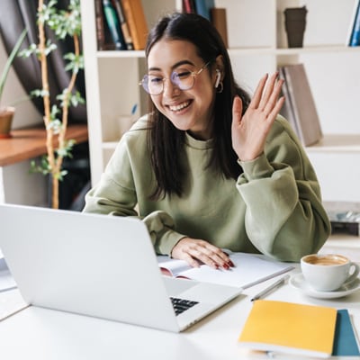 A young teen in a green sweater smiling and waving at the camera while taking an class at Connections Academy. 