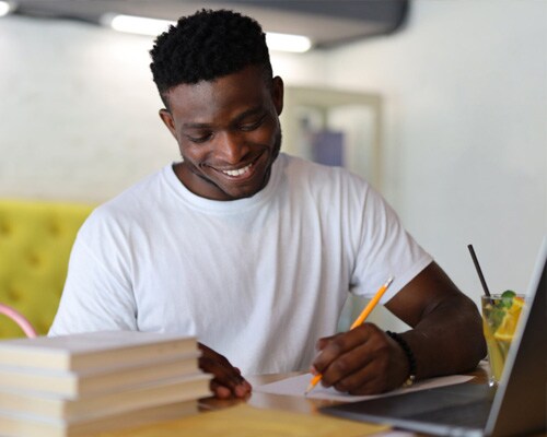 Connections Academy students in a white t-shirt looking at something they are writing down while working on an online assignment.