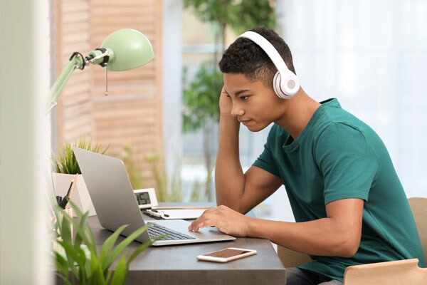 Male teen student in a green t-shirt sitting working on an online assignment for Connections Academy.