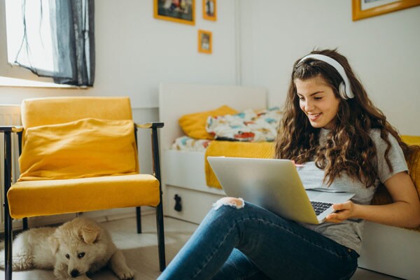 Teen female student in a grey t-shirt sitting against their bed working on an online assignment for Connections Academy.