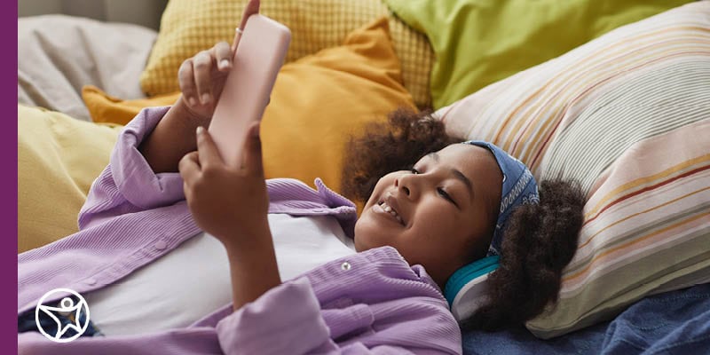 A young girl laying on her bed looking at her phone.