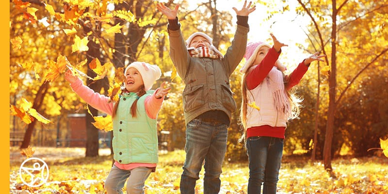 Kids playing outside, throwing fall leaves into the air.