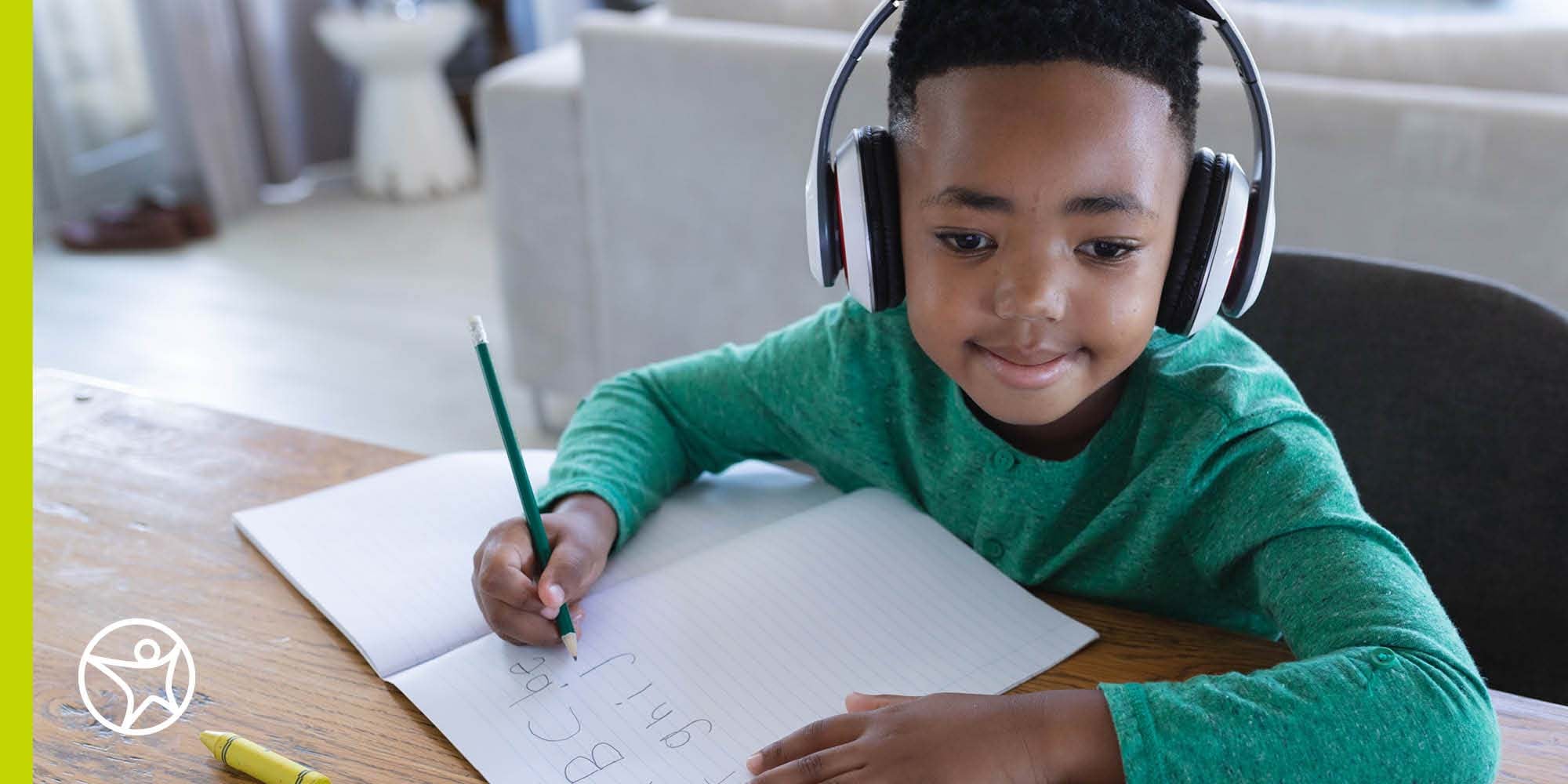 A kindergartner in a green shirt and headphones enjoying his Connections Academy class