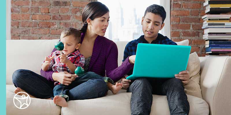 A middle school student with a blue computer working on their laptop while their learning partner holding a baby is helping.