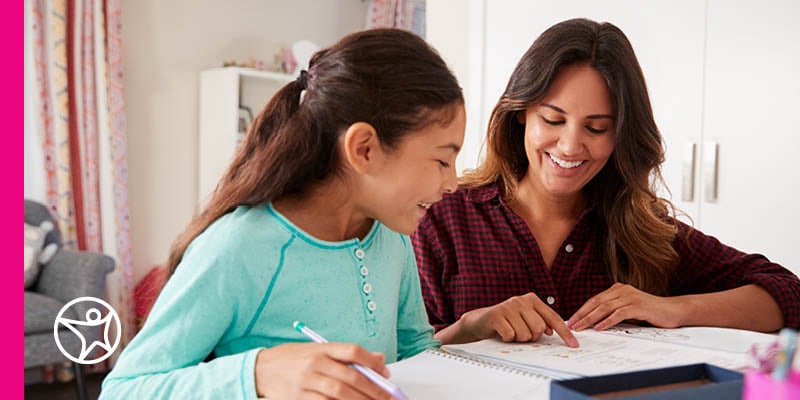 A mother is reading a book with her daughter at a table