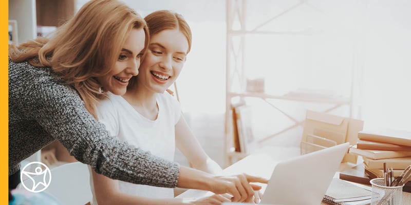 A learning coach in a grey sweater assisting her student in a white t-shirt while on her laptop taking an online class at Connections Academy.