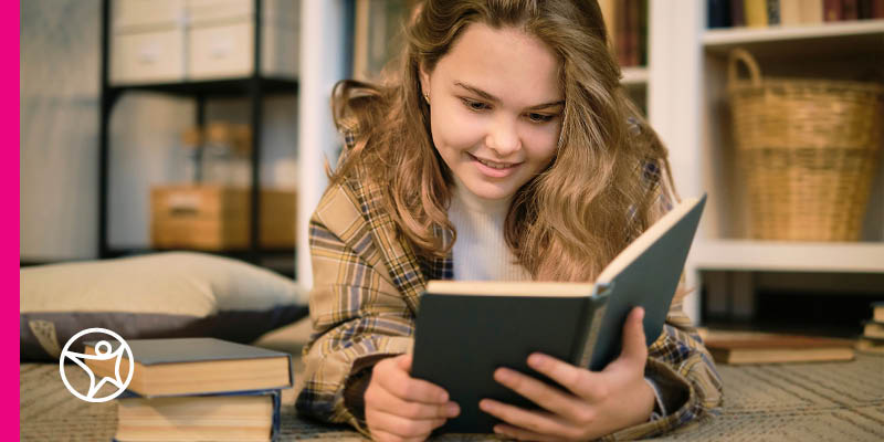 Student reading a book while sitting on a bed