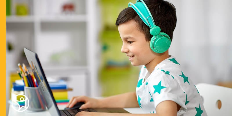 An online school student sitting at a desk wearing headphones and taking part in an online lesson on their laptop
