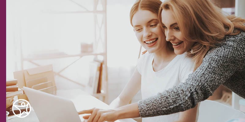 Image of a daughter in a white shirt and mom in a grey sweater working on college applications and finacial aid applications.