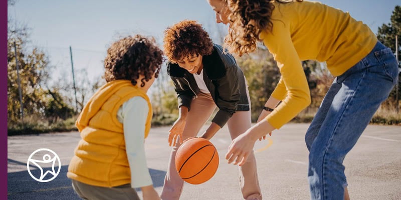 A mother playing basketball with her two sons.