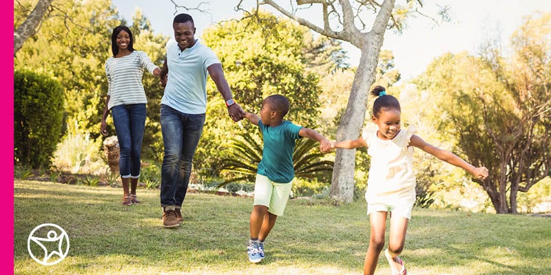 A family of four holding hands and running through a park.
