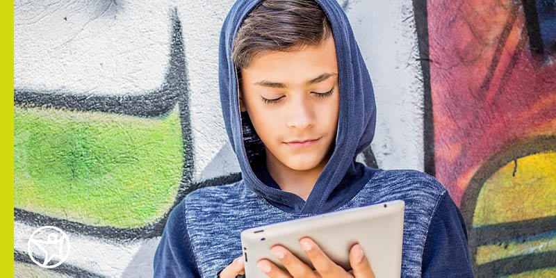 An Oklahoma online school student wearing a blue hoodie and looking down at a tablet in their hands.