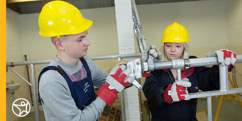 Students wearing hard hats and gloves working with metal pipes.