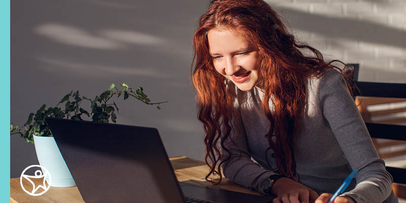 An online high school student looking at her laptop and holding a pen
