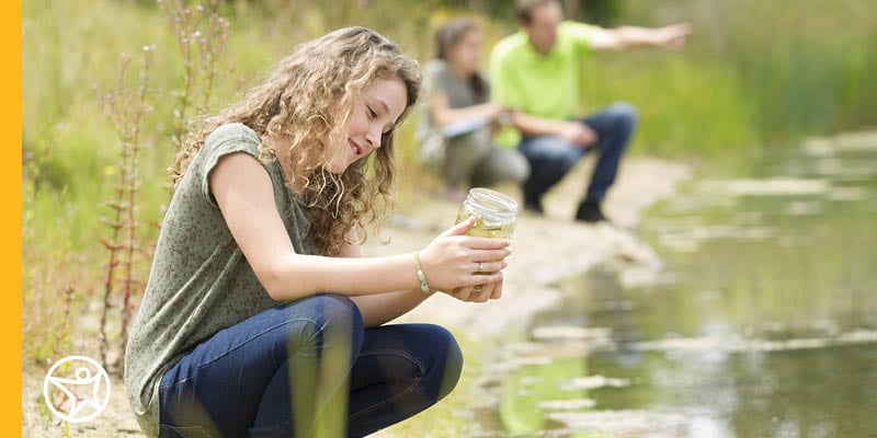 A young girl holding a jar of stream water.