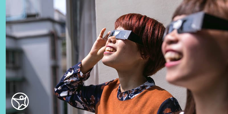 Two online school students looking up at a solar eclipse through special eclipse glasses