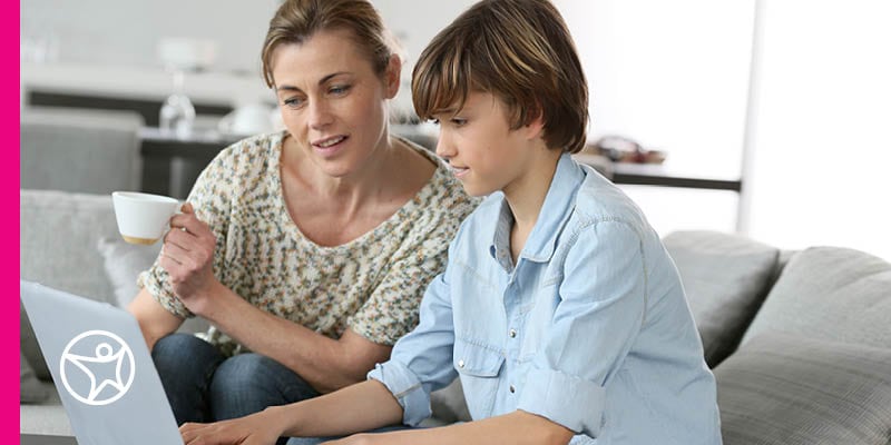 A mother and son learning on a laptop computer while sitting on the couch.