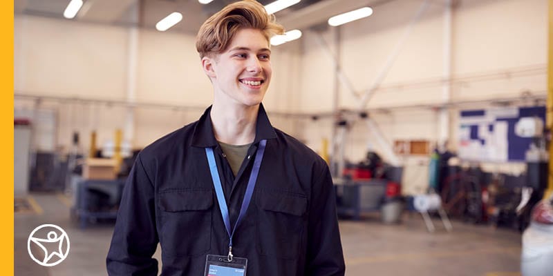 A teenage male student standing in a workshop wearing a name badge.