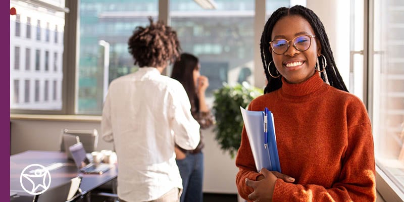 A student in a long sleved red shirt holding a folder and smiling at the camera