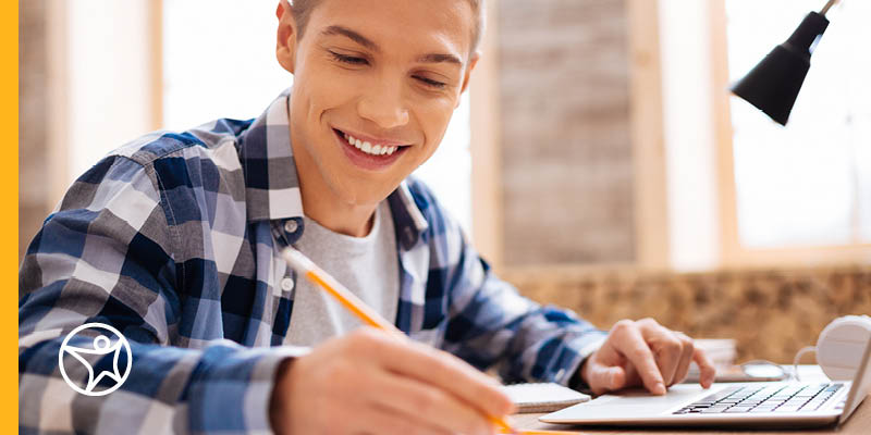 Student studying in a blue plaid shirt taking notes while taking an online class in creative writing.