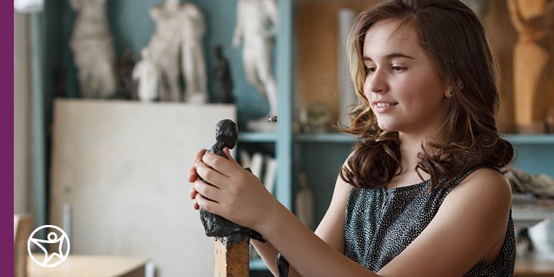 Young female student working on modeling a clay object while taking an art class at a local arts center.